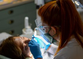 A dentist performing a dental procedure on a patient under bright clinic lights.