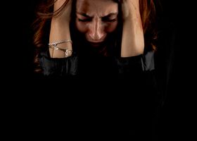 Woman holding head in distress against a dark background, symbolizing emotional struggle.
